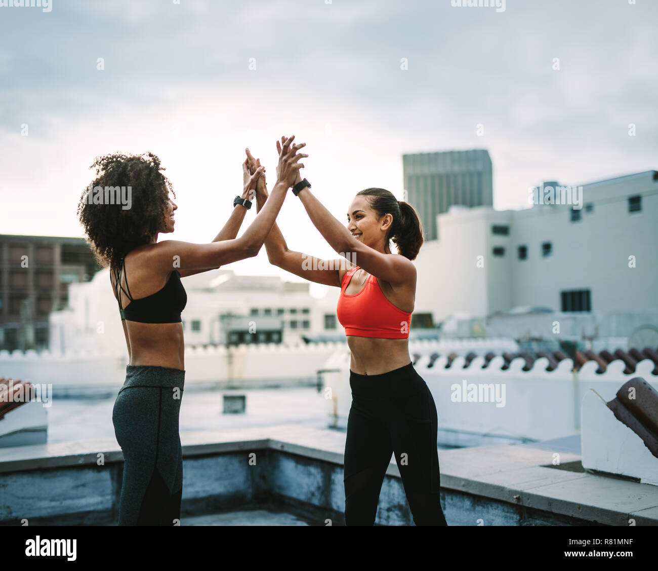 Due donne fitness che festeggiano dando cinque alti dopo l'allenamento. donne che si allenano sul tetto, dando cinque alti con entrambe le mani. Foto Stock