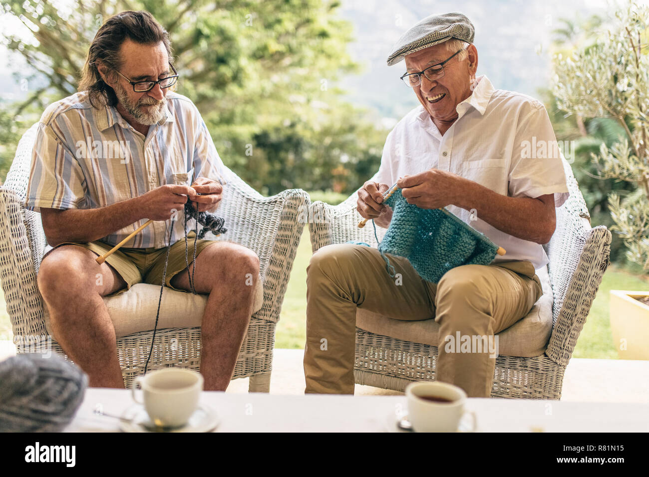 Due alti uomini seduti sulla poltrona e maglia. Maschio in pensione amici facendo maglia per passatempo a casa. Foto Stock