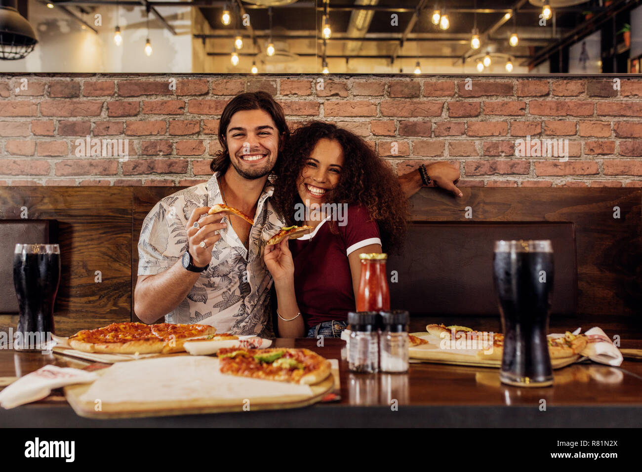 Ritratto di felice coppia giovane seduto insieme al ristorante con il trancio di pizza in mano. Uomo sorridente e donna seduta al cafe con pizza sul tavolo. Foto Stock