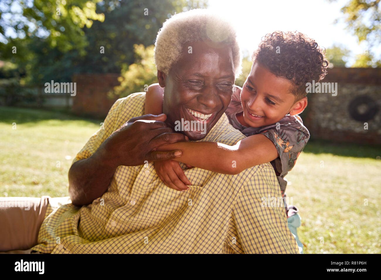 Senior uomo nero seduto su erba, abbracciato dal nipote Foto Stock