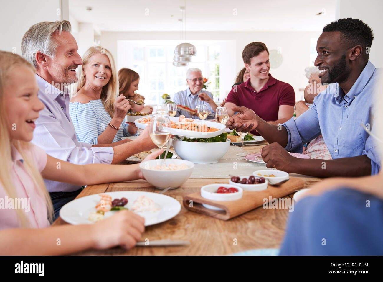 Gruppo di Multi-Generation la famiglia e gli amici seduti attorno al tavolo e godendo di pasto Foto Stock