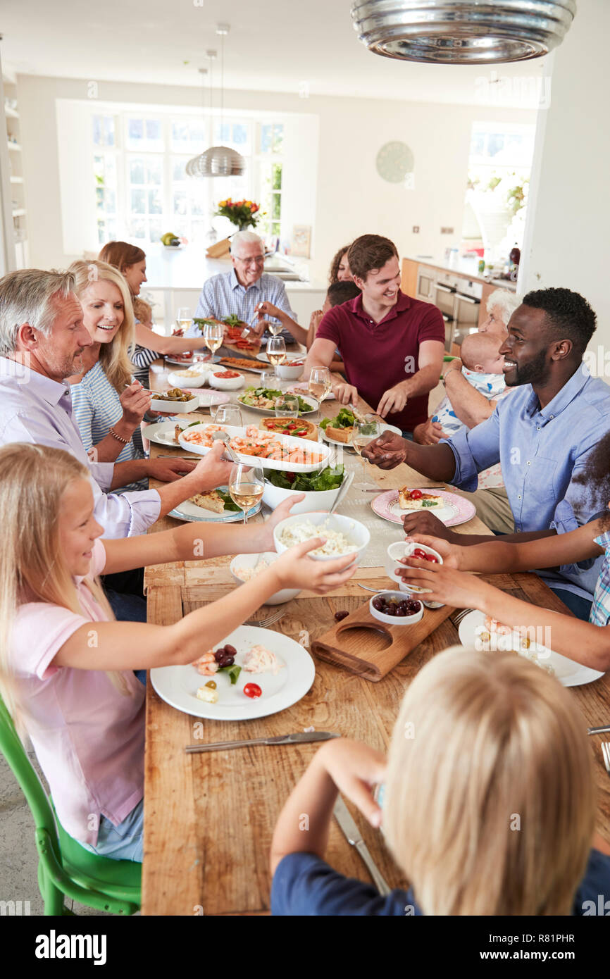Gruppo di Multi-Generation la famiglia e gli amici seduti attorno al tavolo e godendo di pasto Foto Stock