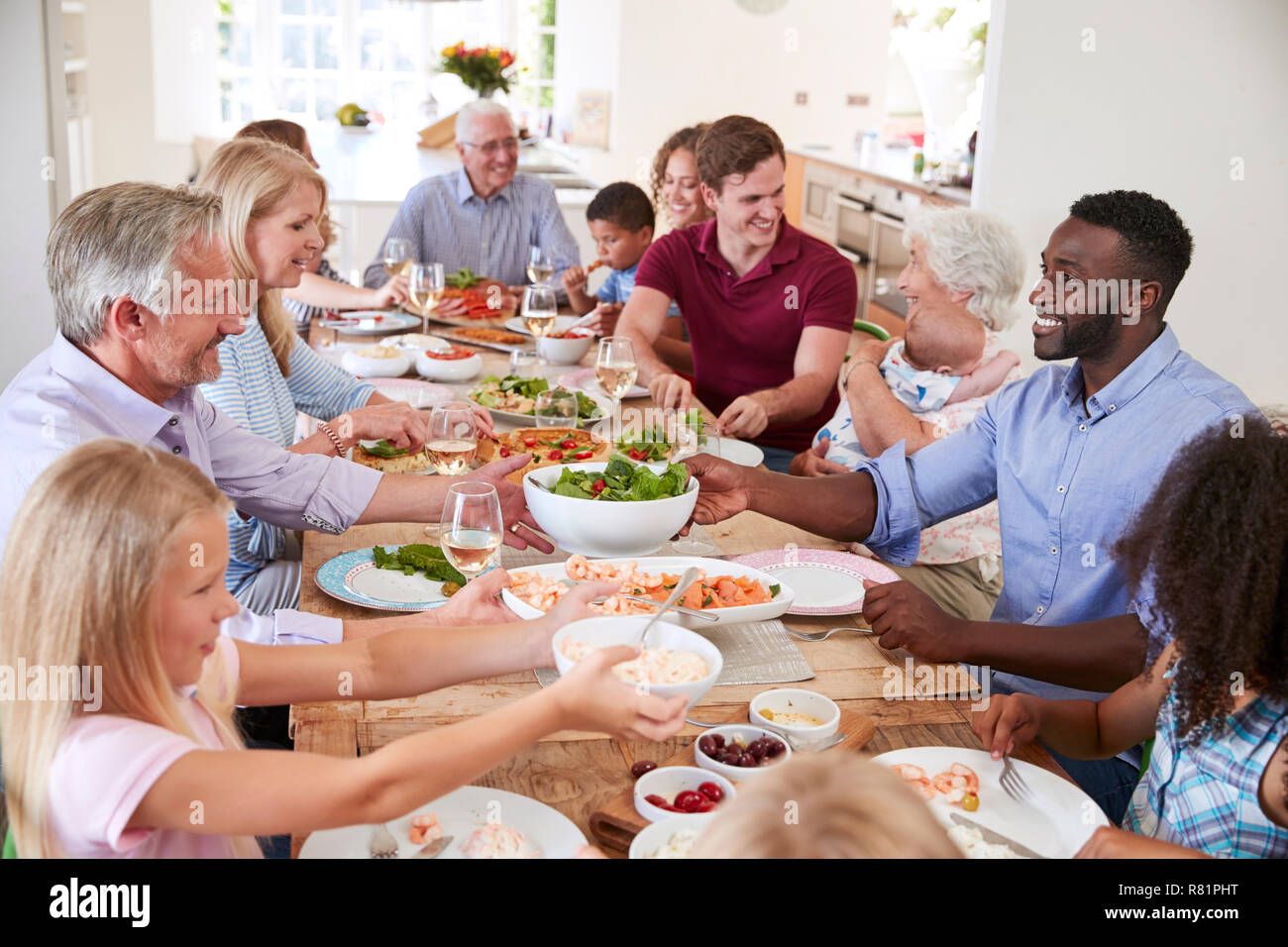 Gruppo di Multi-Generation la famiglia e gli amici seduti attorno al tavolo e godendo di pasto Foto Stock