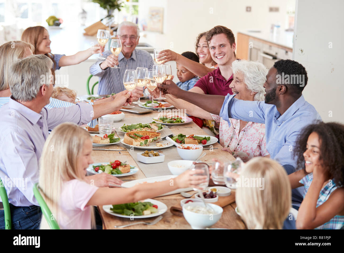 Gruppo di Multi-Generation la famiglia e gli amici seduti attorno al tavolo e fare un brindisi Foto Stock