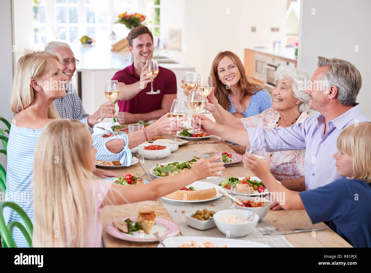 Gruppo di Multi-Generation la famiglia e gli amici seduti attorno al tavolo e fare un brindisi Foto Stock