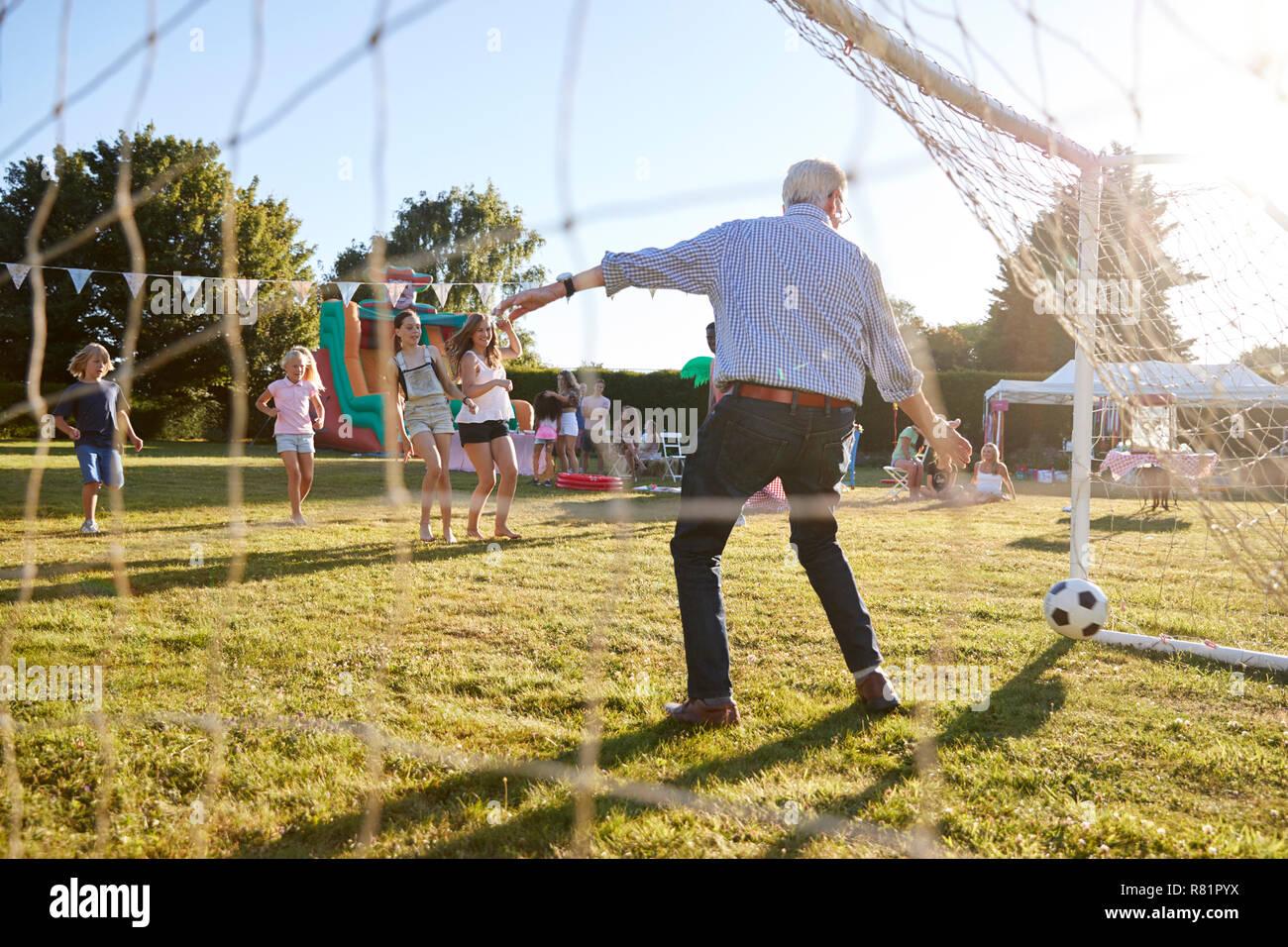 Bambini che giocano una partita di calcio con i Senior Man a giardino estivo Fete Foto Stock