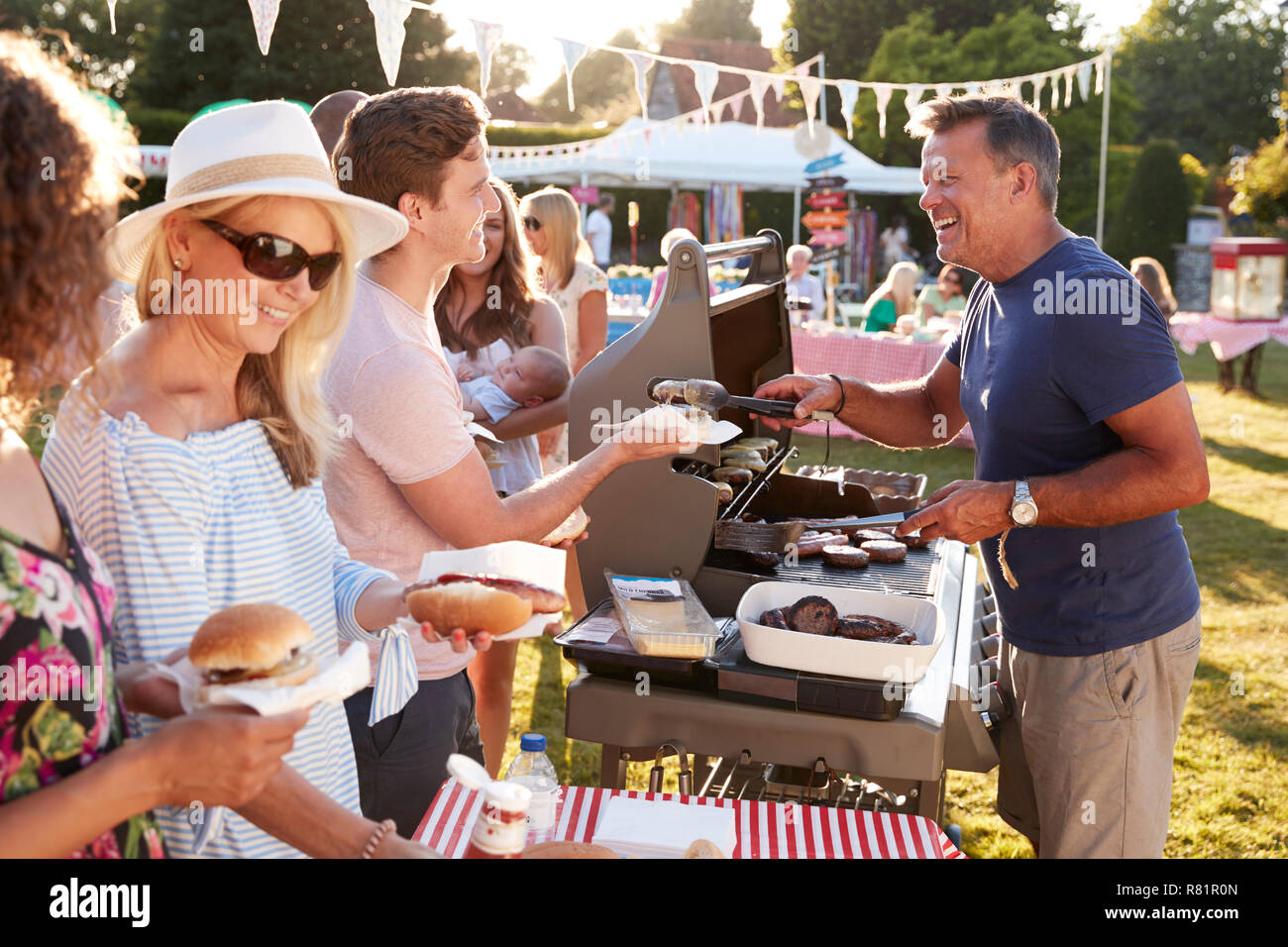 Uomo che serve sul barbeque stallo a giardino estivo Fete Foto Stock