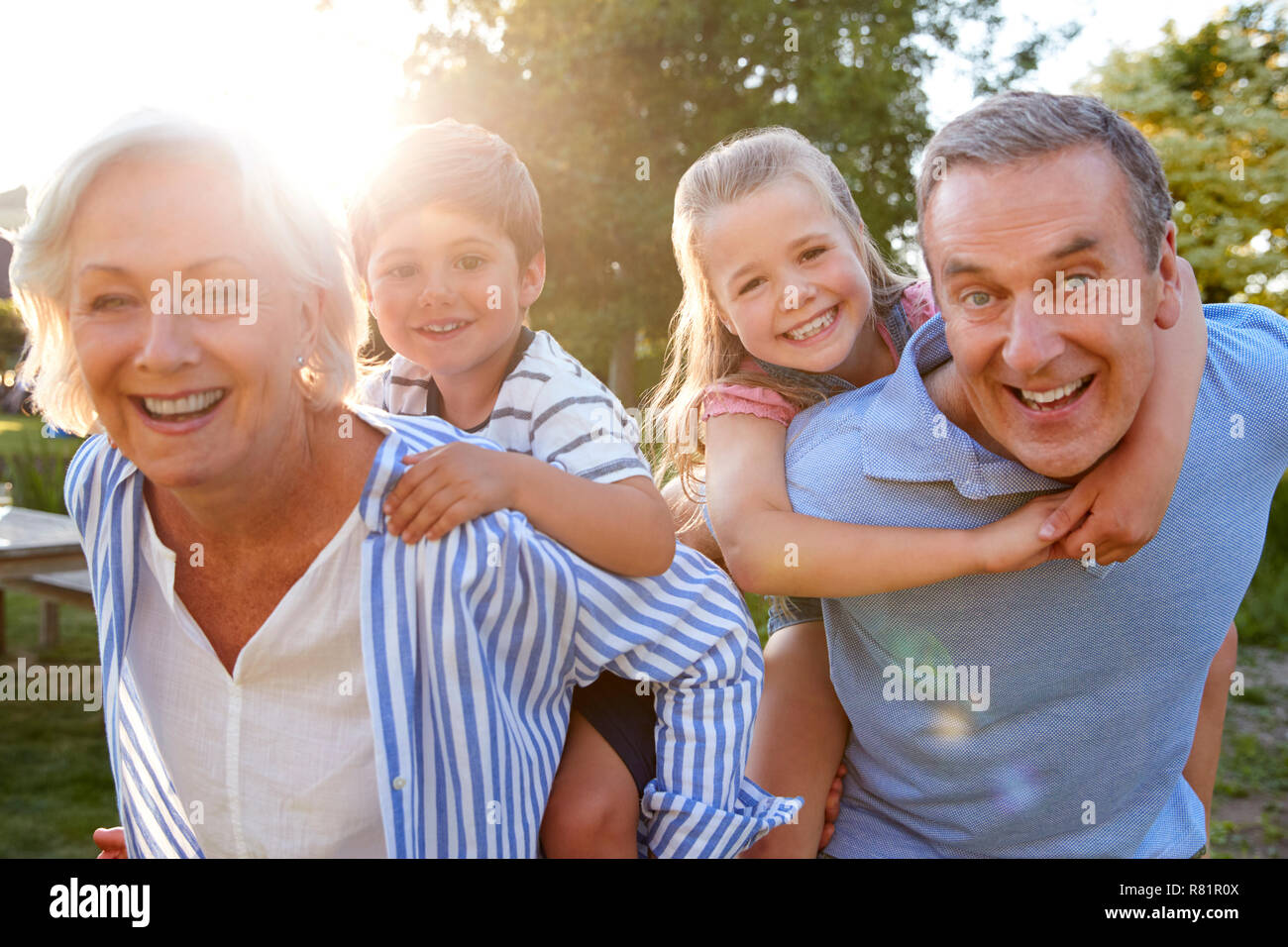 Ritratto di sorridere i nonni dando nipoti Piggyback Ride all'aperto in estate Park Foto Stock