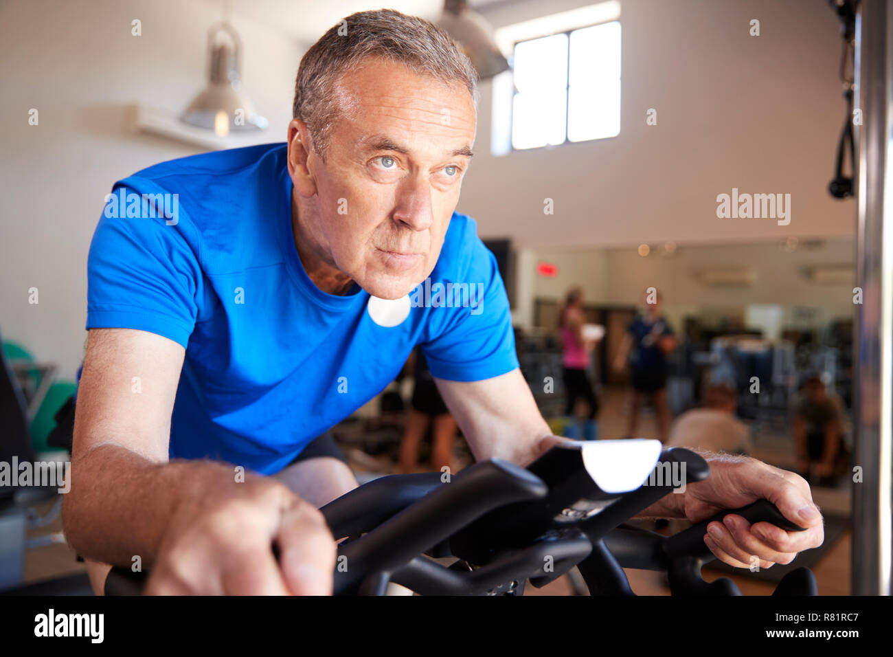 Senior uomo esercita sulla macchina in bicicletta in palestra Foto Stock