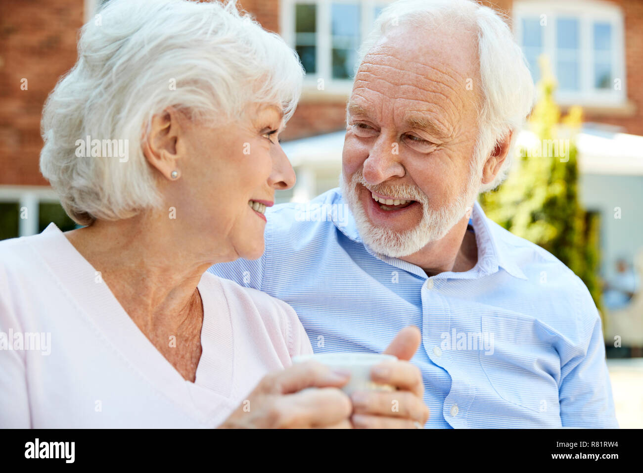 Coppia in pensione seduta sul banco di lavoro con una bevanda calda In Assisted Living Facility Foto Stock