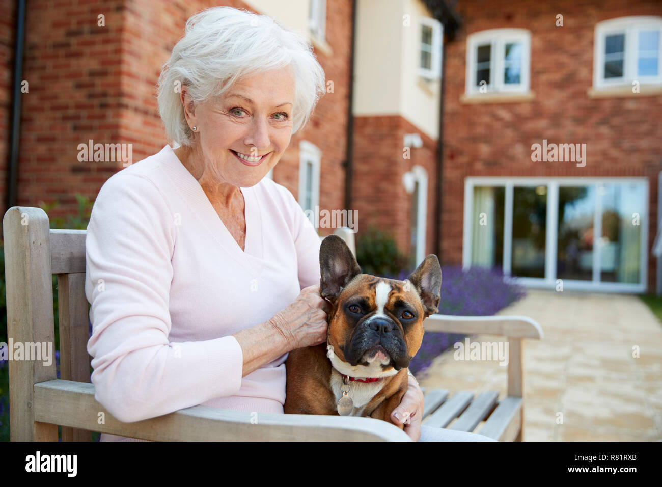 Ritratto di Senior donna seduta su un banco di lavoro con Pet bulldog francese in Assisted Living Facility Foto Stock