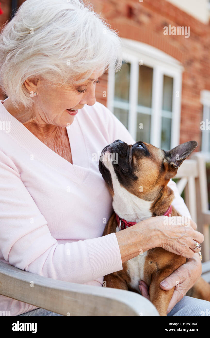 Senior donna seduta su un banco di lavoro con Pet bulldog francese in Assisted Living Facility Foto Stock