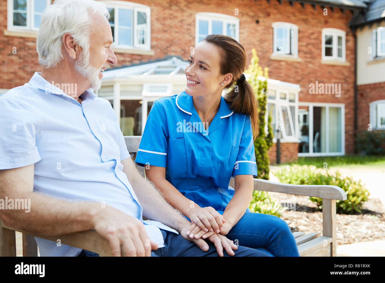Senior uomo seduto su un banco di lavoro e parlare con un infermiere in casa di riposo Foto Stock