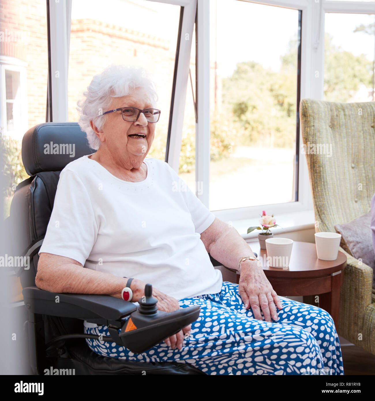 Senior donna seduta nel salotto della casa di riposo in sedia a rotelle motorizzata Foto Stock