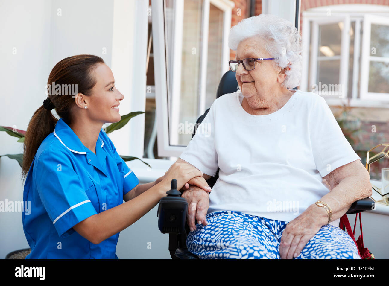 Senior donna seduta in sedia a rotelle motorizzata a parlare con un infermiere in casa di riposo Foto Stock