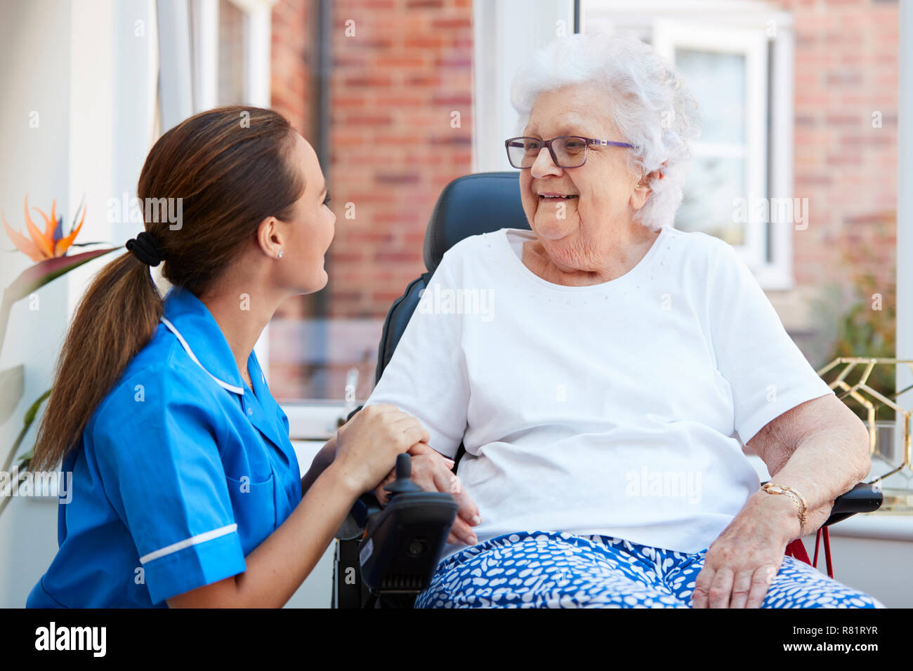 Senior donna seduta in sedia a rotelle motorizzata a parlare con un infermiere in casa di riposo Foto Stock