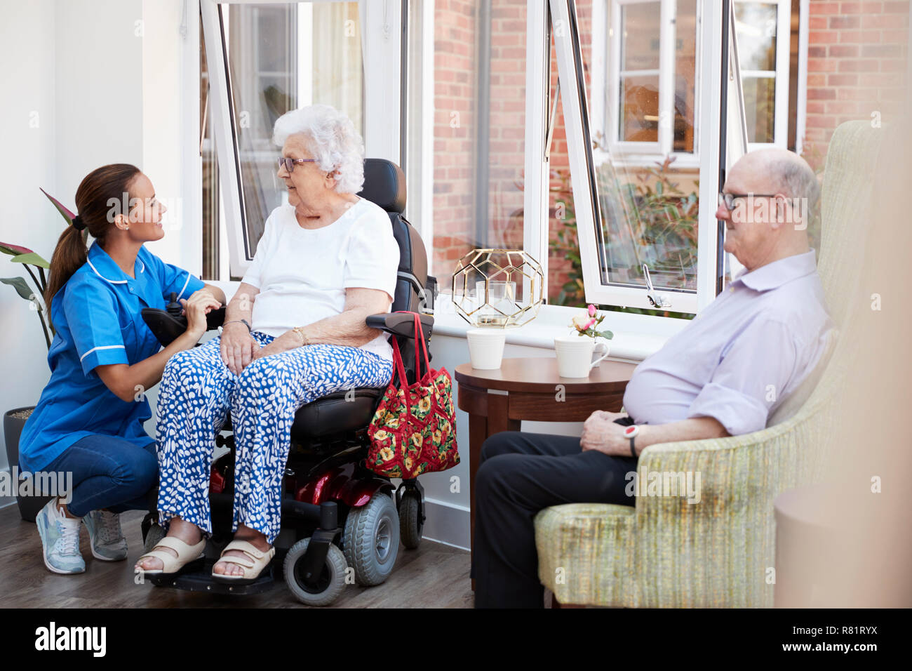 Maschio e femmina residenti seduto in poltrona e parlare con un infermiere in casa di riposo Foto Stock