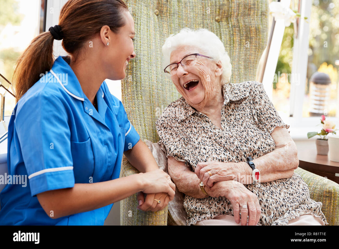Senior donna seduta in poltrona e ridere con infermiere in casa di riposo Foto Stock