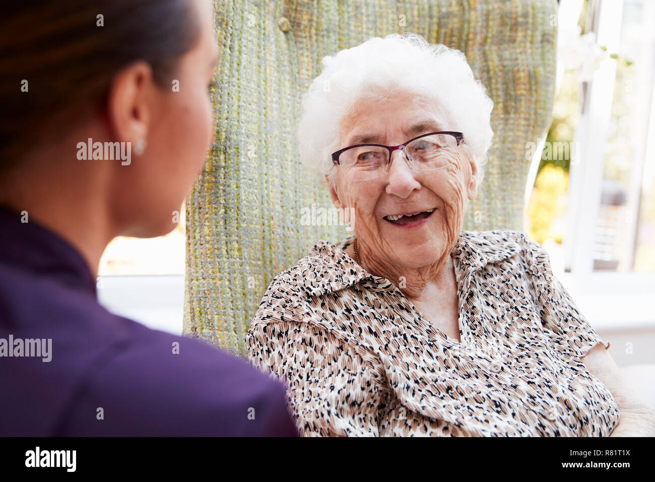 Residente femmina seduto in poltrona e parlando con accompagnatore in casa di riposo Foto Stock