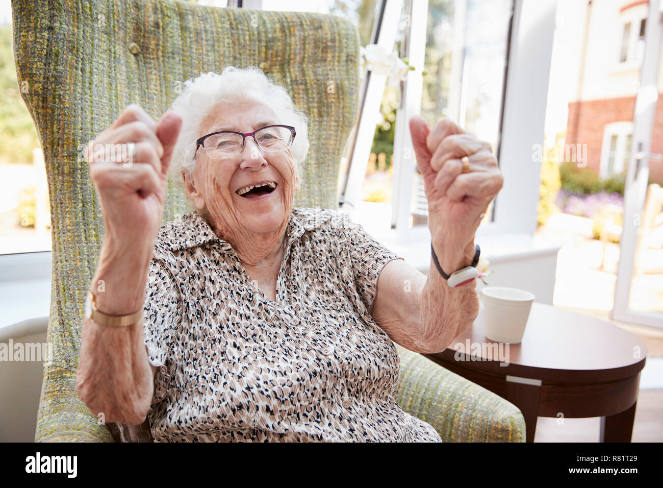 Ritratto di entusiasti Senior donna seduta in poltrona nel salotto di casa di riposo Foto Stock