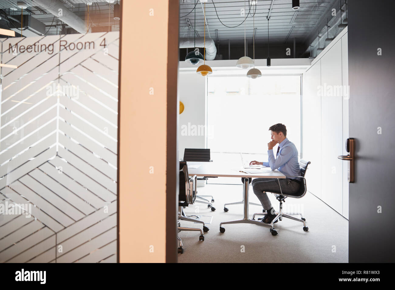 Imprenditore lavora su computer portatile al Tavolo per riunioni visto attraverso la Sala Riunioni porta Foto Stock