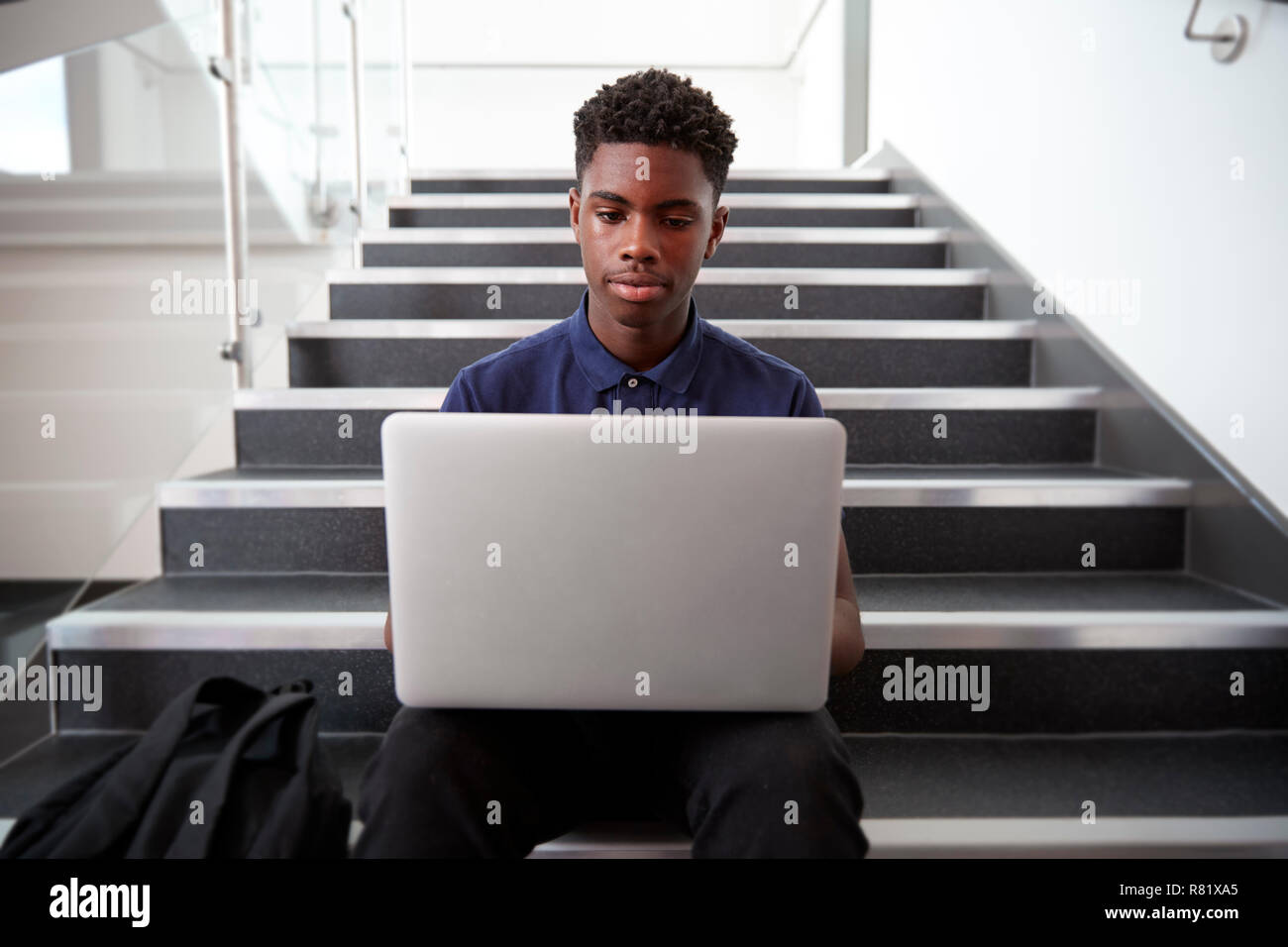 Maschio di alta scuola studente seduto sulla scalinata e utilizzando computer portatile Foto Stock