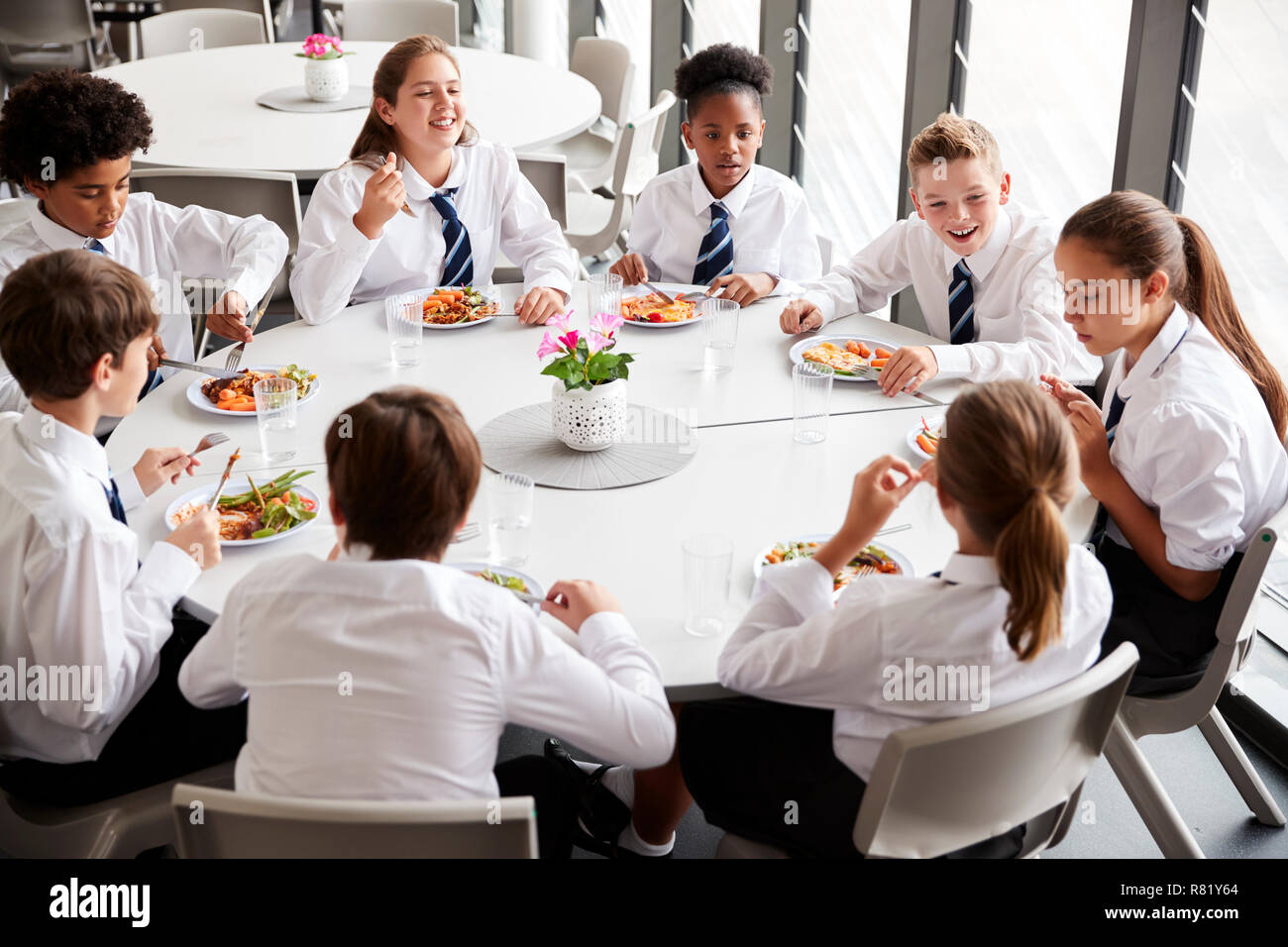 Un gruppo di studenti di scuola superiore che indossano uniformi di sedersi a tavola e mangiare il pranzo nella caffetteria Foto Stock