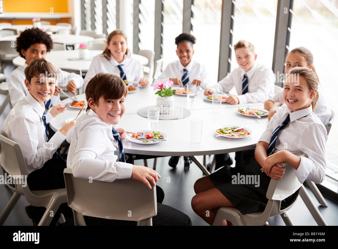 Ritratto di alta scuola gli studenti indossano uniformi di sedersi a tavola e mangiare il pranzo nella caffetteria Foto Stock
