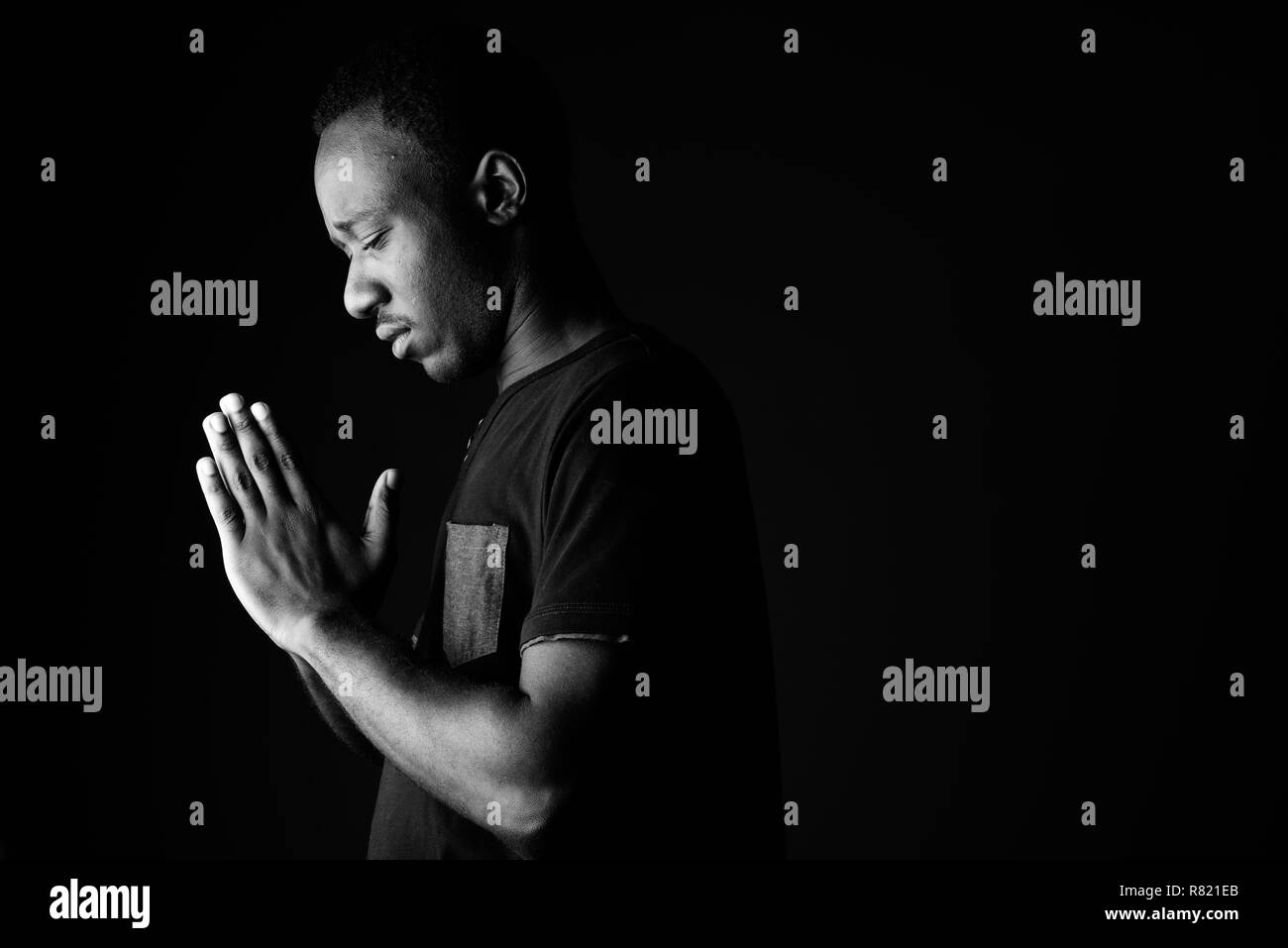 Triste giovane africano pregando in bianco e nero Foto Stock