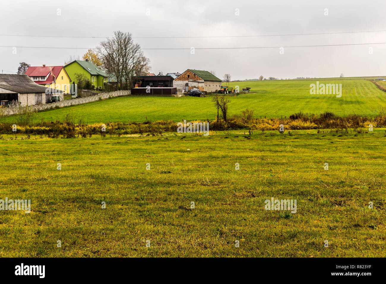 Il tardo autunno.Il verde dei prati che circondano il villaggio in primo piano.case e edifici agricoli in background. Sito circa agroindustria,meteo, stagioni . Foto Stock