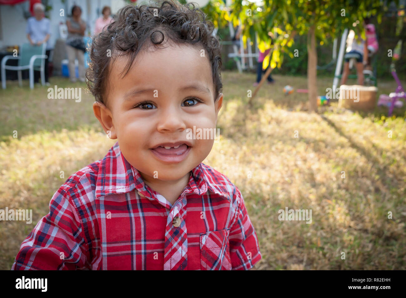 Felice-anno-vecchio ragazzo guardando la telecamera con un sorriso. Vista dettagliata del toddler boy a piedi per fotocamera a una festa di famiglia nel cortile. Foto Stock