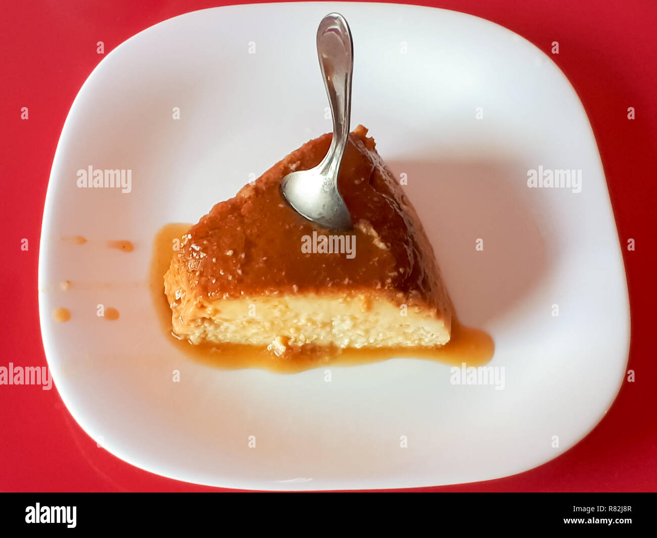 Un gustoso pezzo di pudding con sciroppo di zucchero su una piastra bianca e un cucchiaio bloccato sul suo lato superiore Foto Stock