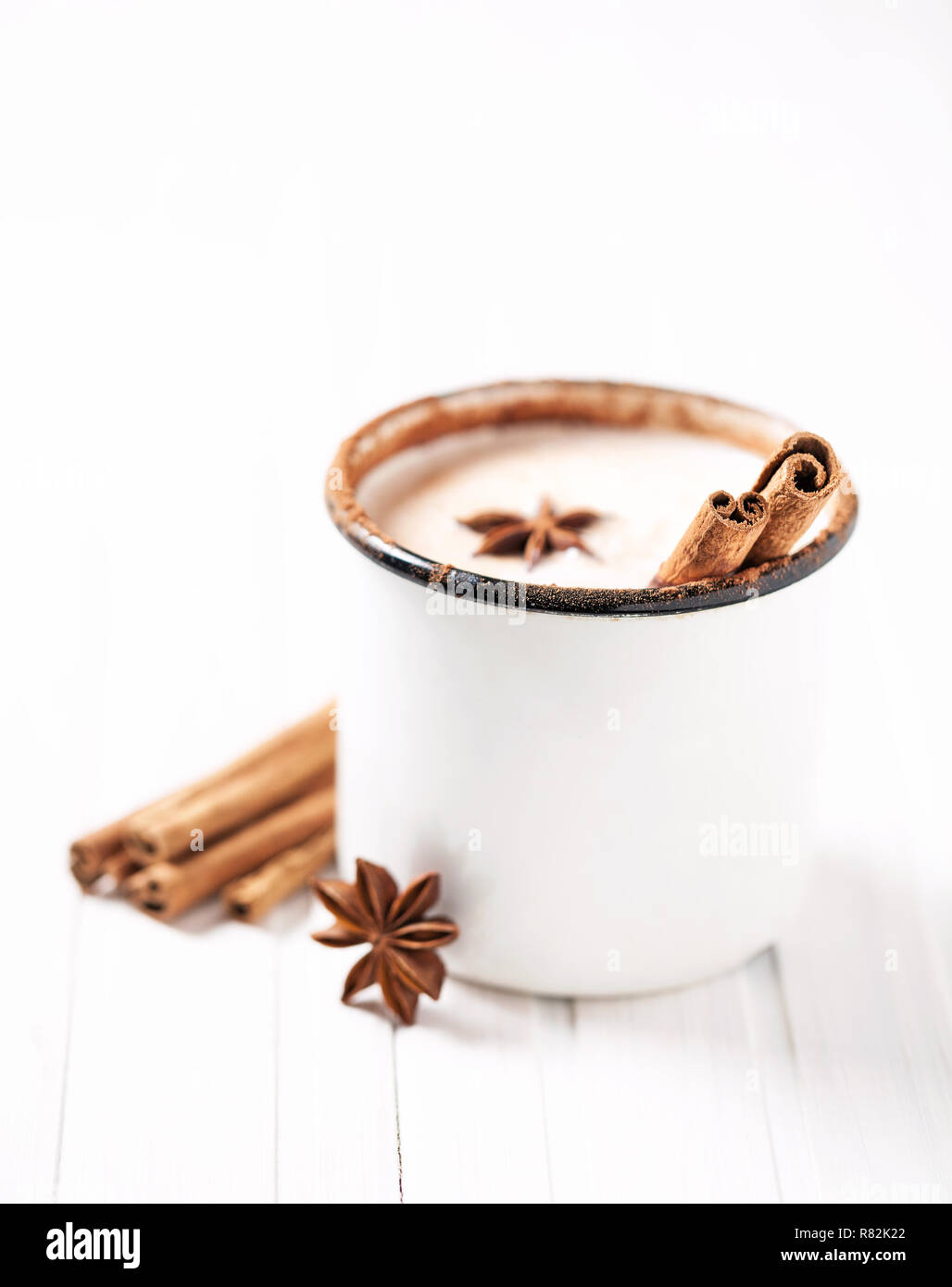 Latte con cannella e anice in tazza rustico su bianco tavolo in legno Foto Stock