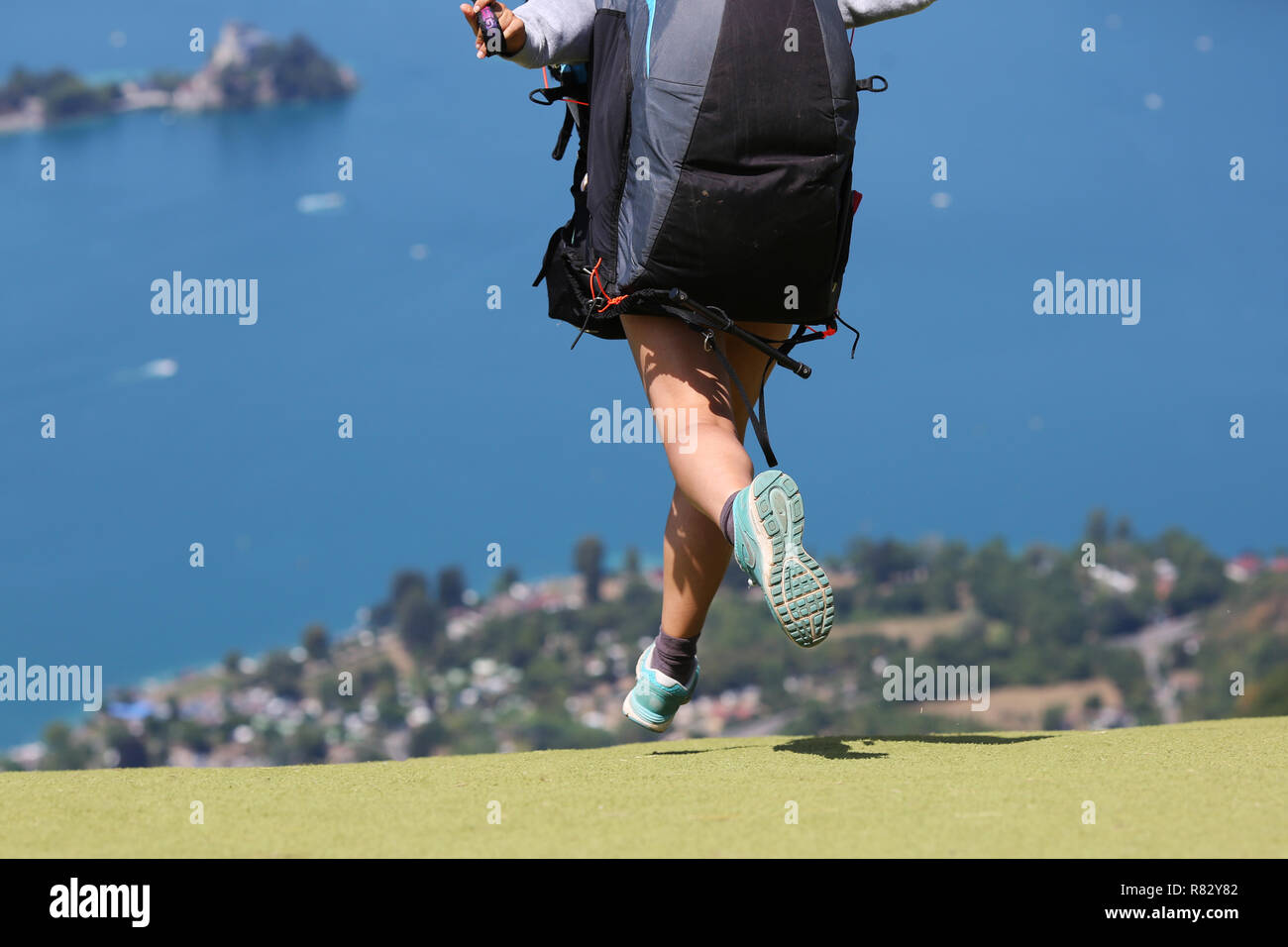 Una femmina di pilota di parapendio decollo al Col de la Forclaz, vicino a Annecy, Francia, con il lago di Annecy in background. Foto Stock