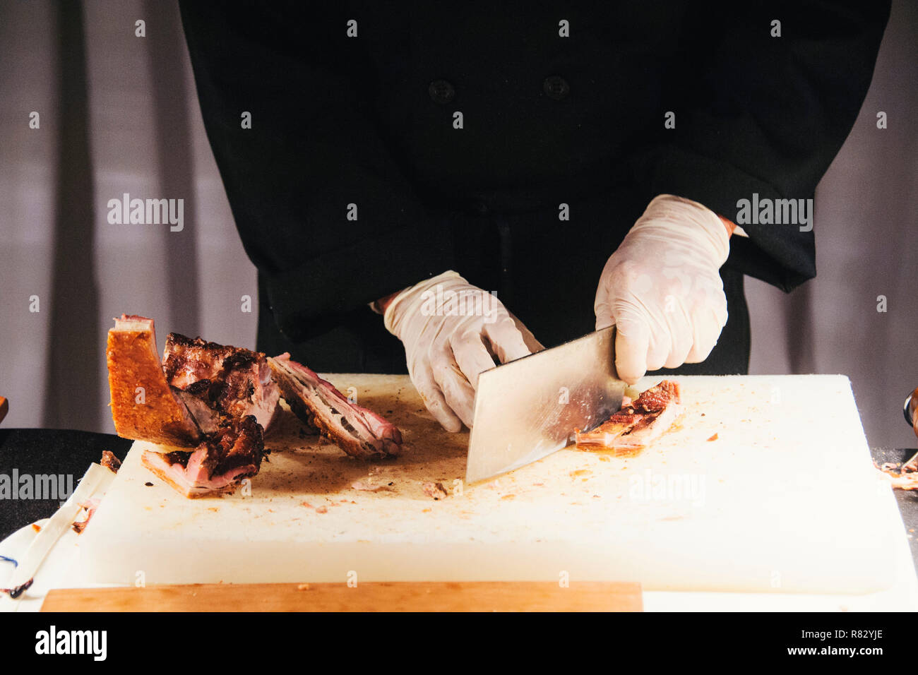 Le mani di un maschio di costolette di maiale arrosto con una mannaia a una festa Foto Stock