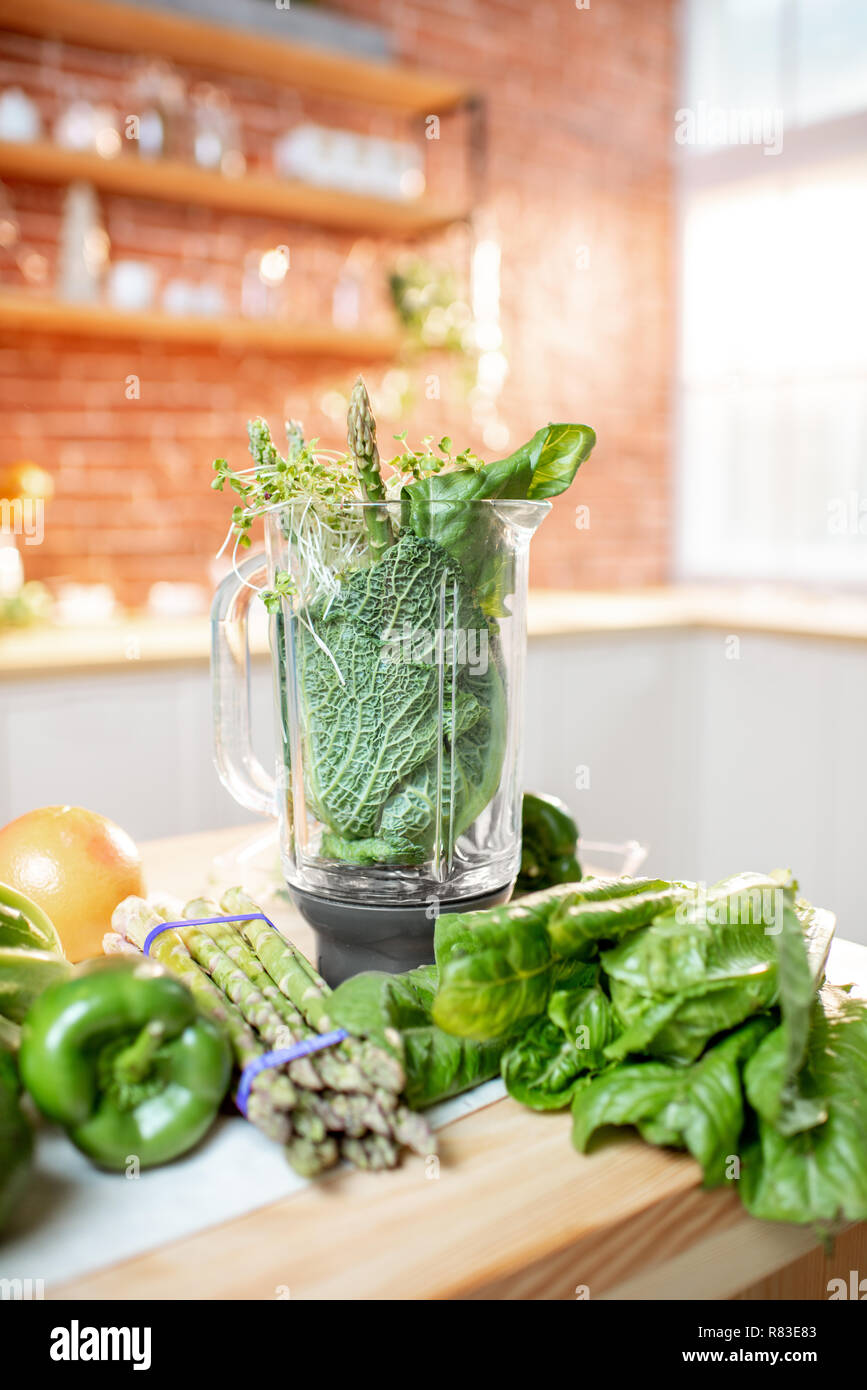 Frullatore pieno di ingredienti per rendere frullato sul tavolo verde con verdure crude in cucina Foto Stock