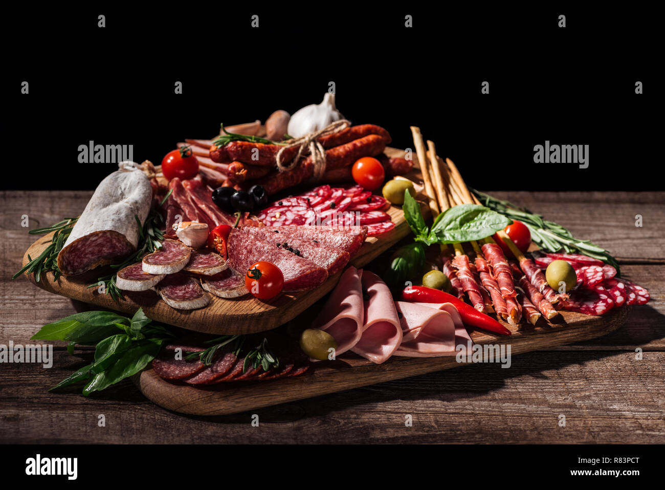 Schede di taglio con deliziosi salami, salsicce affumicate, prosciutto, le verdure e le erbe in legno tavolo rustico Foto Stock