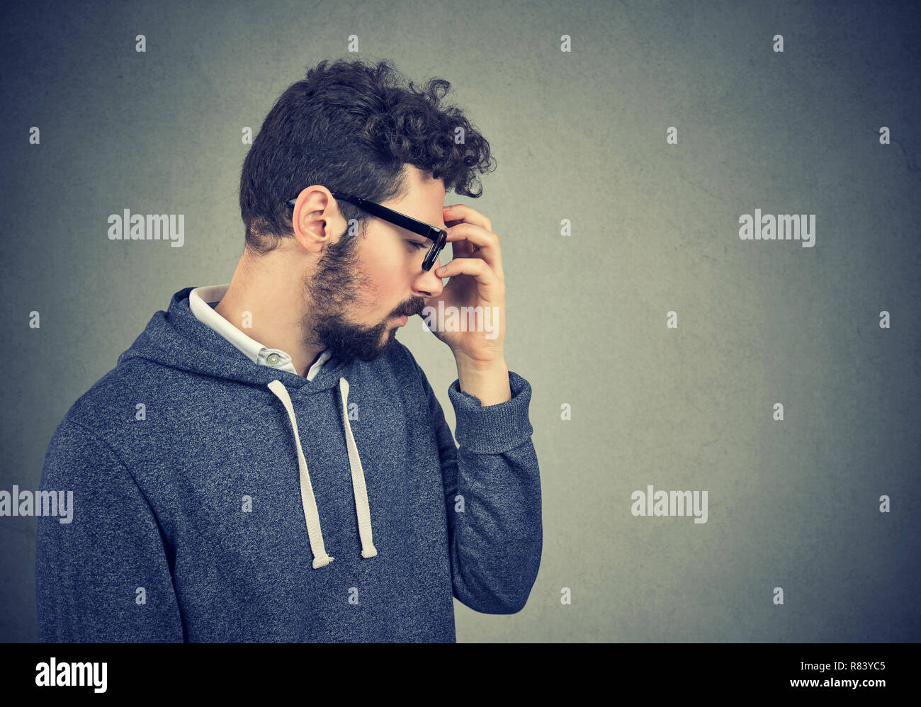 Profilo laterale di un uomo in felpa con cappuccio casual tenendo la mano sulla fronte in disperazione e consapevolezza Foto Stock