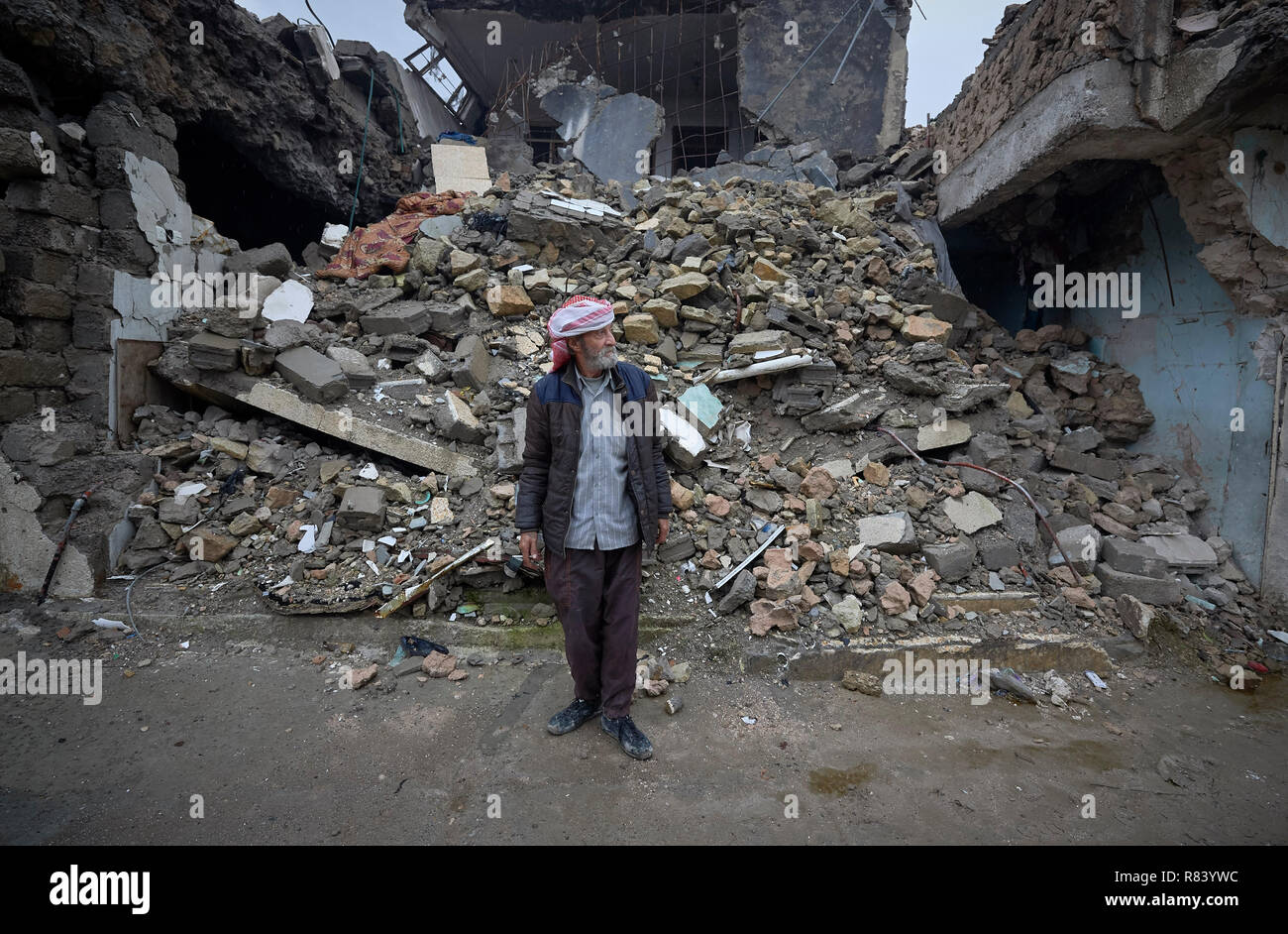 Qasim Yahia Ali, 75, vive nella vecchia città di Mosul, Iraq. La sua casa dietro di lui è stata distrutta durante il 2017 Battaglia di Mosul. Foto Stock