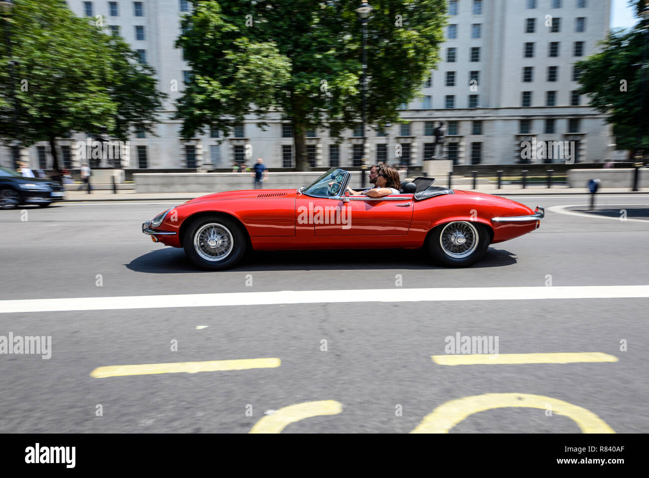 Open top E-type Jaguar guidando lungo Whitehall a Londra, Regno Unito. Classic Vintage Jaguar cabriolet E Tipo auto. Rosso. Parte superiore verso il basso. MoD Headquarters Building Foto Stock