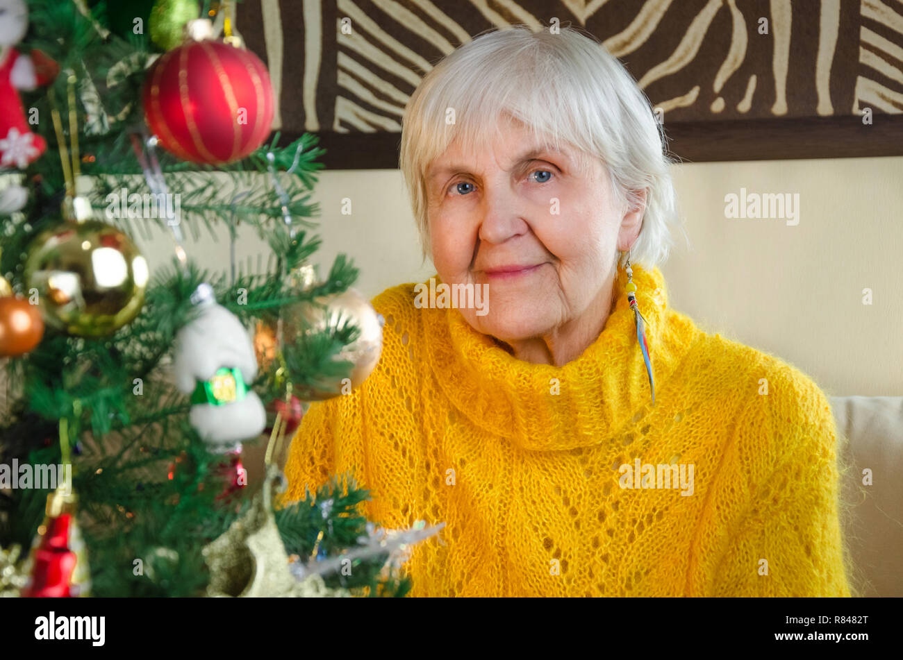 Ritratto di vecchia nonna a casa nel nuovo anno positivo caucasici, friendly granny in festosa, bianco maglia maglione. anziani donna accogliente vicino a Natale, albero. senior lady guardano alla fotocamera. Foto Stock