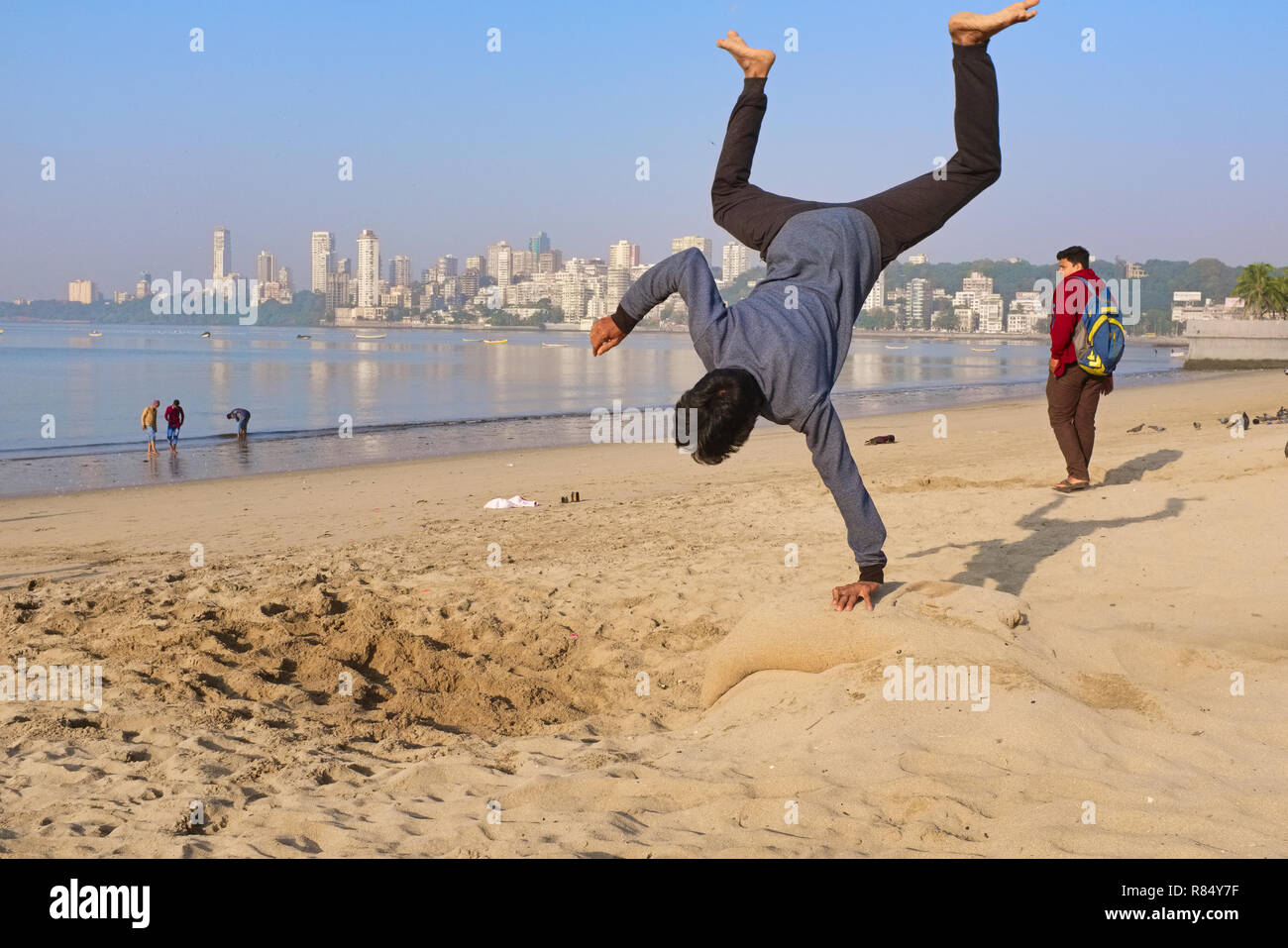 Un giovane uomo sulla spiaggia dal Mare arabico off Marine Drive, Mumbai, India, praticando salti mortali come parte di una routine di danza Foto Stock