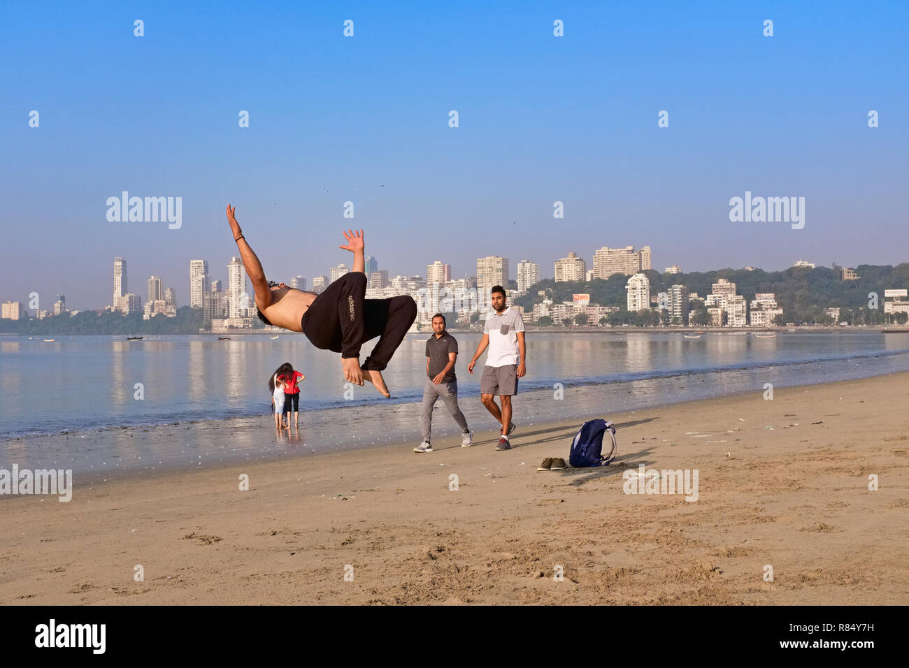 Un giovane uomo sulla spiaggia dal Mare arabico off Marine Drive, Mumbai, India, praticando salti mortali come parte di una routine di danza Foto Stock