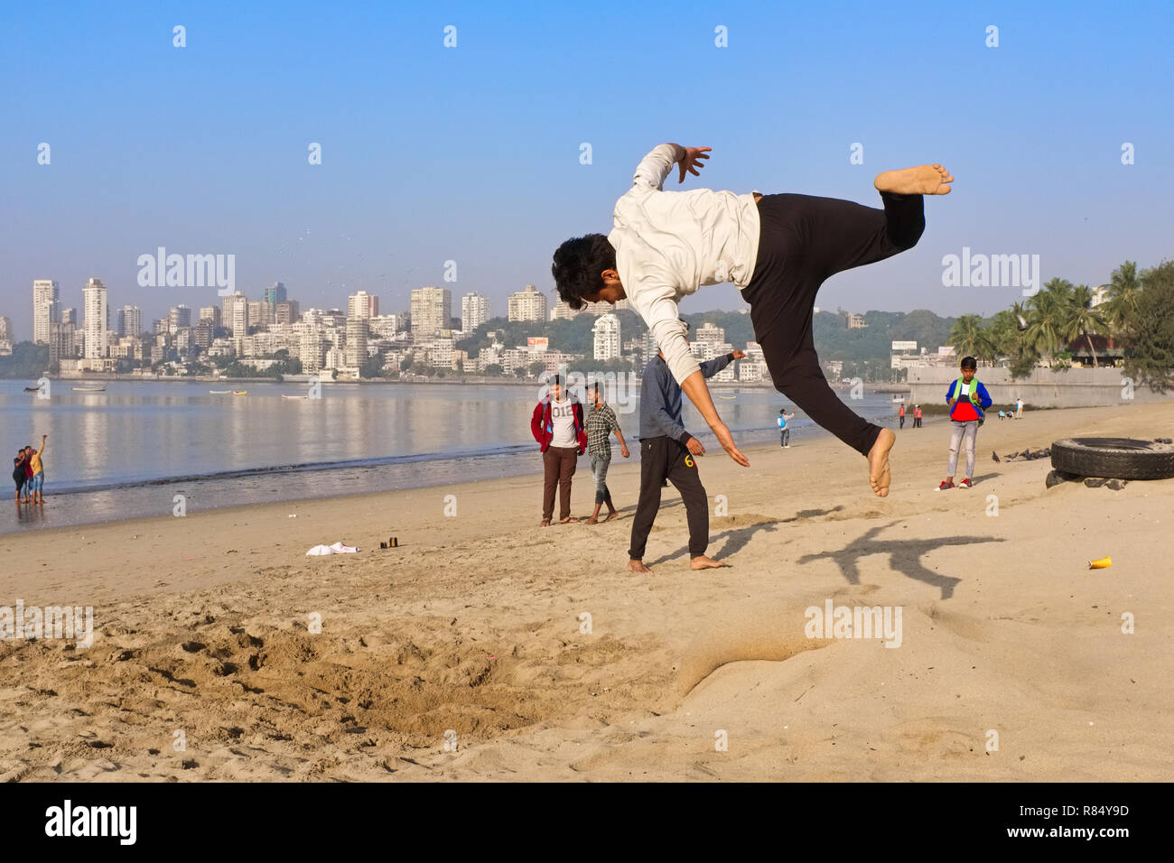 Un giovane uomo sulla spiaggia dal Mare arabico off Marine Drive, Mumbai, India, praticando salti mortali come parte di una routine di danza Foto Stock