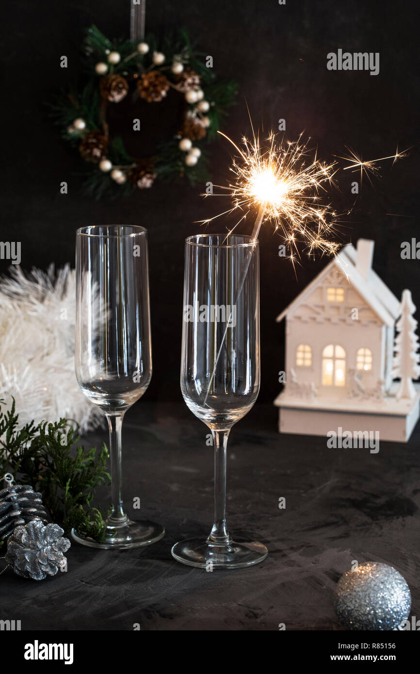 Due bicchieri vuoti per lo champagne con sparkler a sfondo nero, tinsel e Natale giocattolo vicino Foto Stock