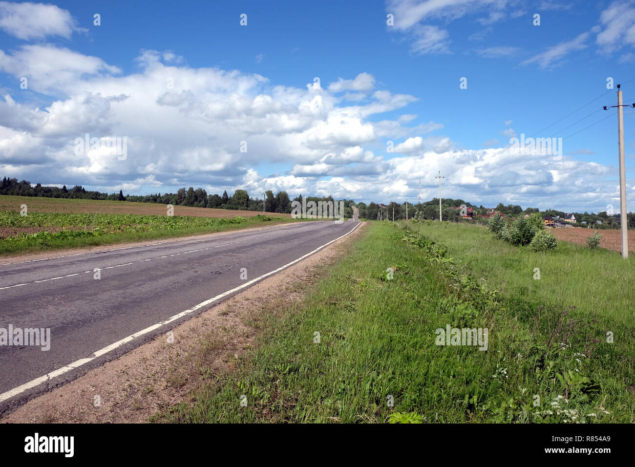 Paesaggio di campagna con il russo strada asfaltata di scarsa qualità rientranti nella distanza in direzione del villaggio nella soleggiata giornata estiva Foto Stock