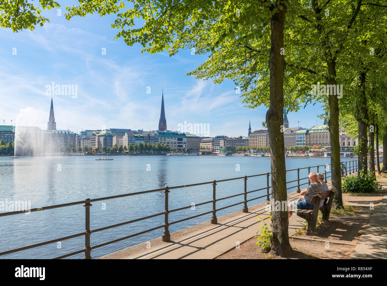 Coppia seduta su una panchina sulle rive del lago Binnenalster con lo skyline della città dietro, Amburgo, Germania Foto Stock