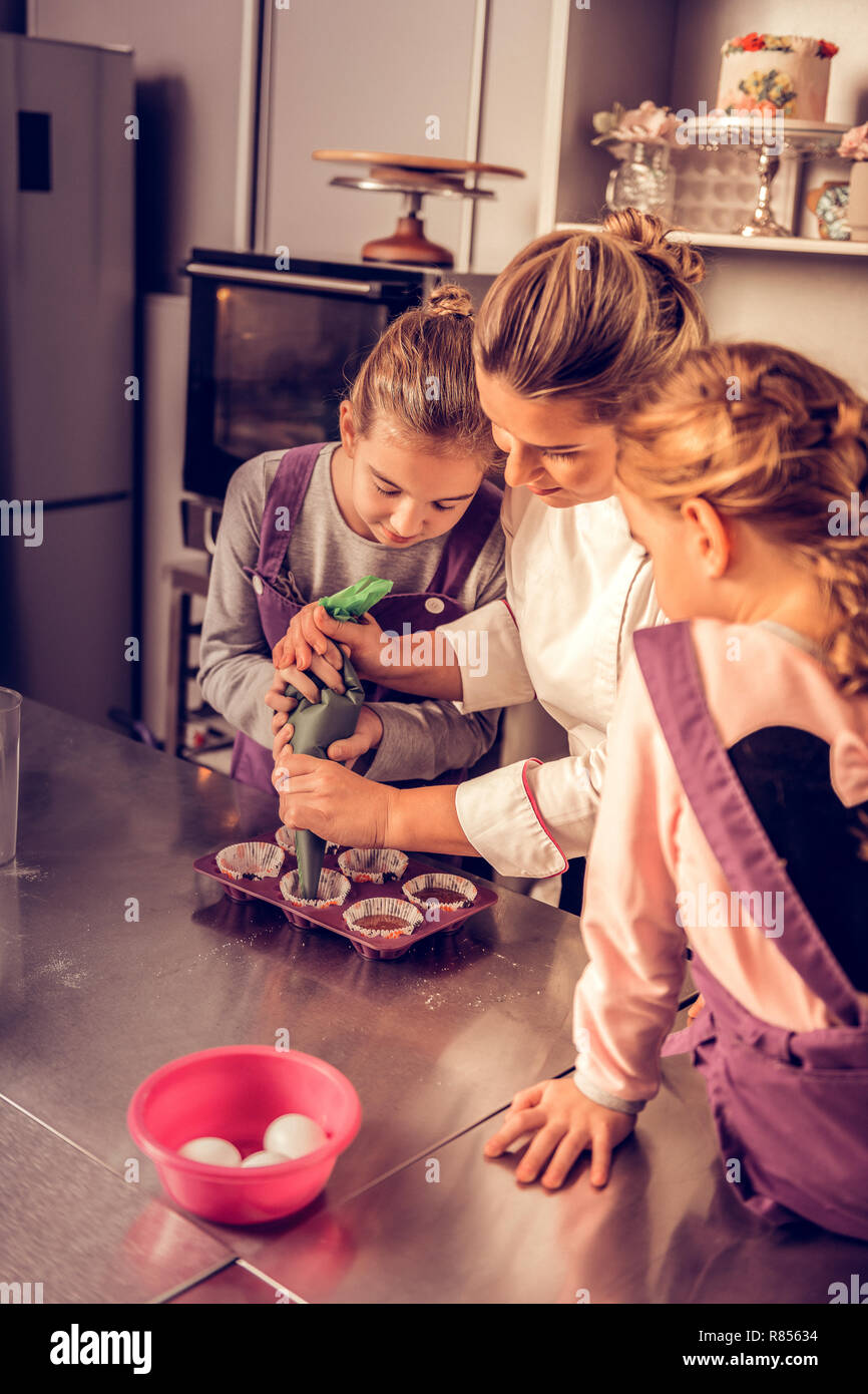 Lezione aperta. Professional esperti donna in piedi con due ragazze mentre mostrando loro una specialità culinaria master class Foto Stock
