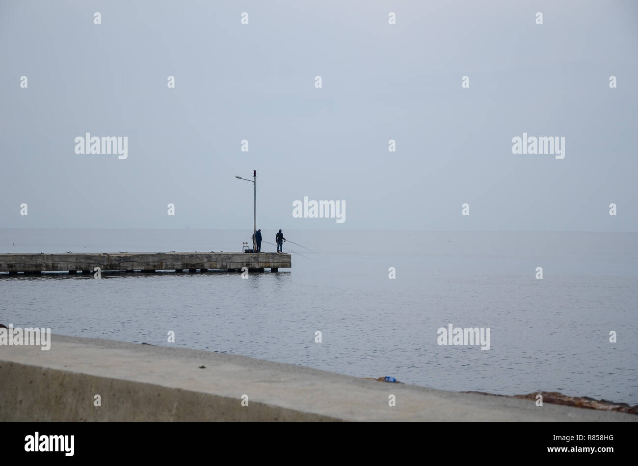 Tre pescatori sono in piedi e la pesca in mare Foto Stock