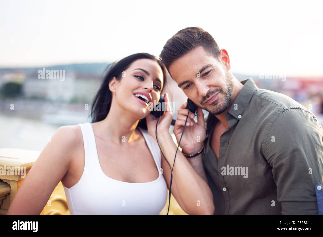 Urban paio di cuffie di condivisione e ascolto di musica a all'aperto in sunset Foto Stock
